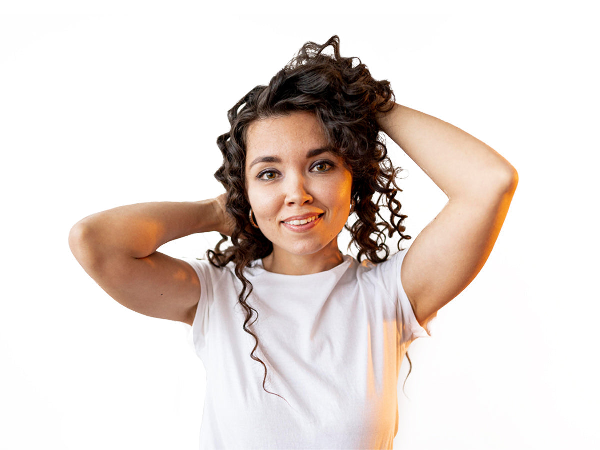 Smiling woman with defined dark curls and her hands in her hair, low porosity hair care