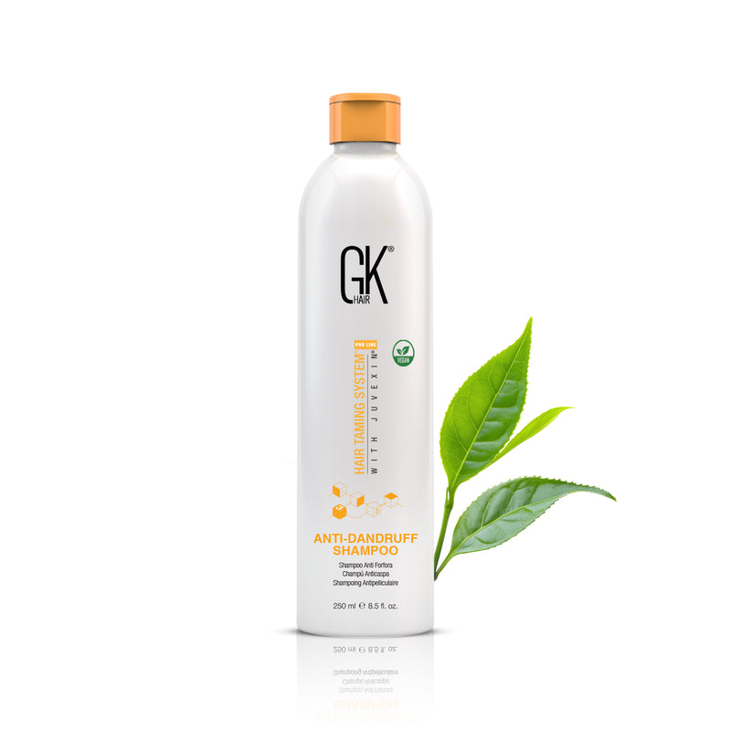 GK Hair Anti-Dandruff Shampoo 250 ml vegan bottle with an orange cap, green tea leaves beside it on a white background