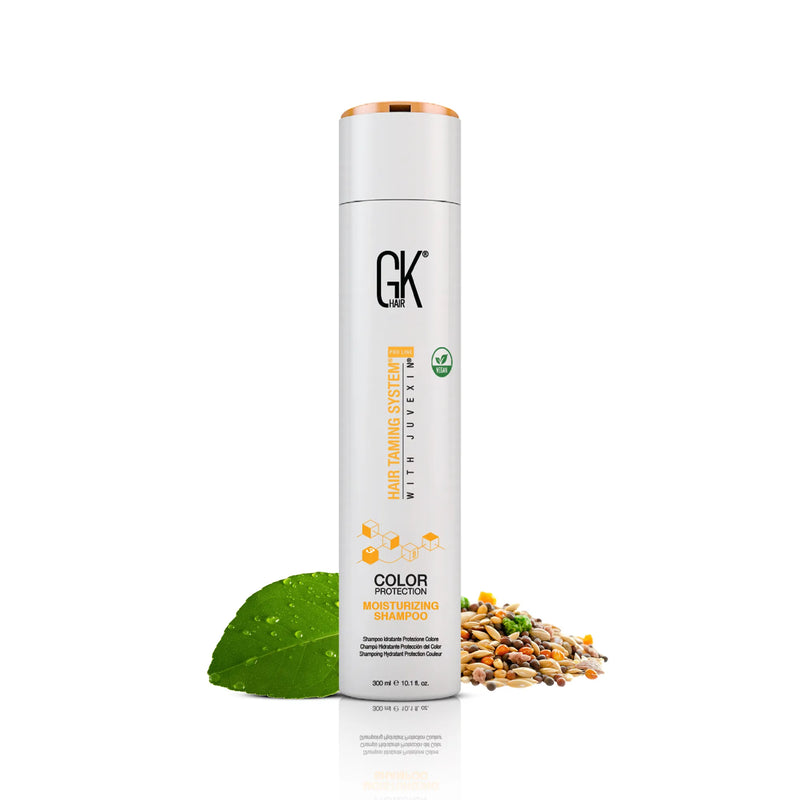 GK Hair Moisturizing Shampoo 300 ml white bottle with a copper cap, front view, next to a dewy green leaf and scattered grains